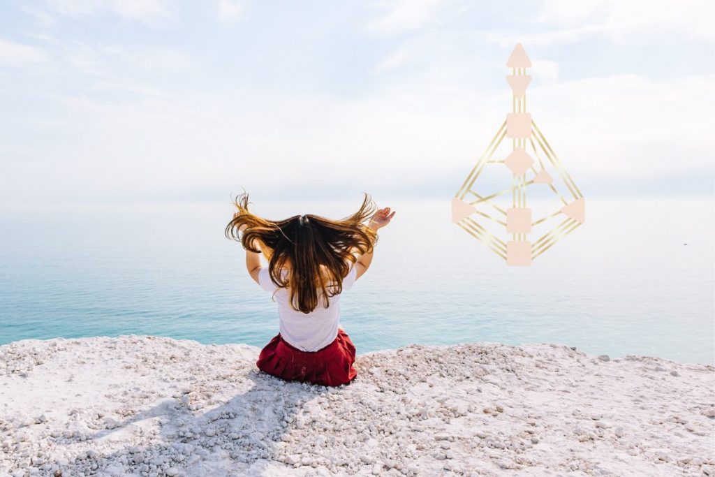 Frau sitzt mit dem Rücken zum Betrachtenden auf dem Boden und sieht auf das Meer.