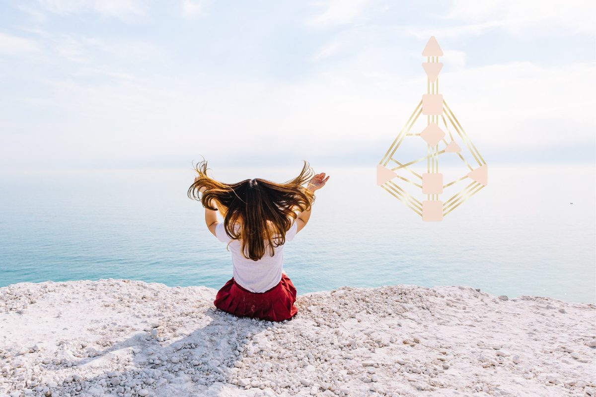 Frau sitzt mit dem Rücken zum Betrachtenden auf dem Boden und sieht auf das Meer.