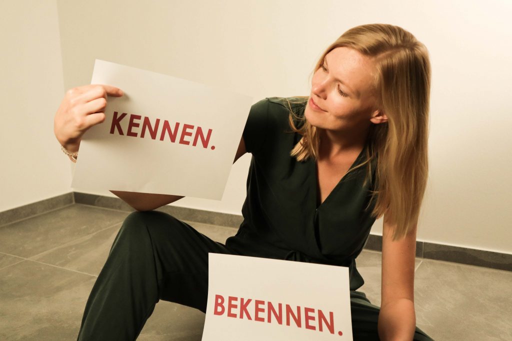 blonde Frau mit zwei Schildern in der Hand, auf denen "Kennen" und "Bekennen" steht
